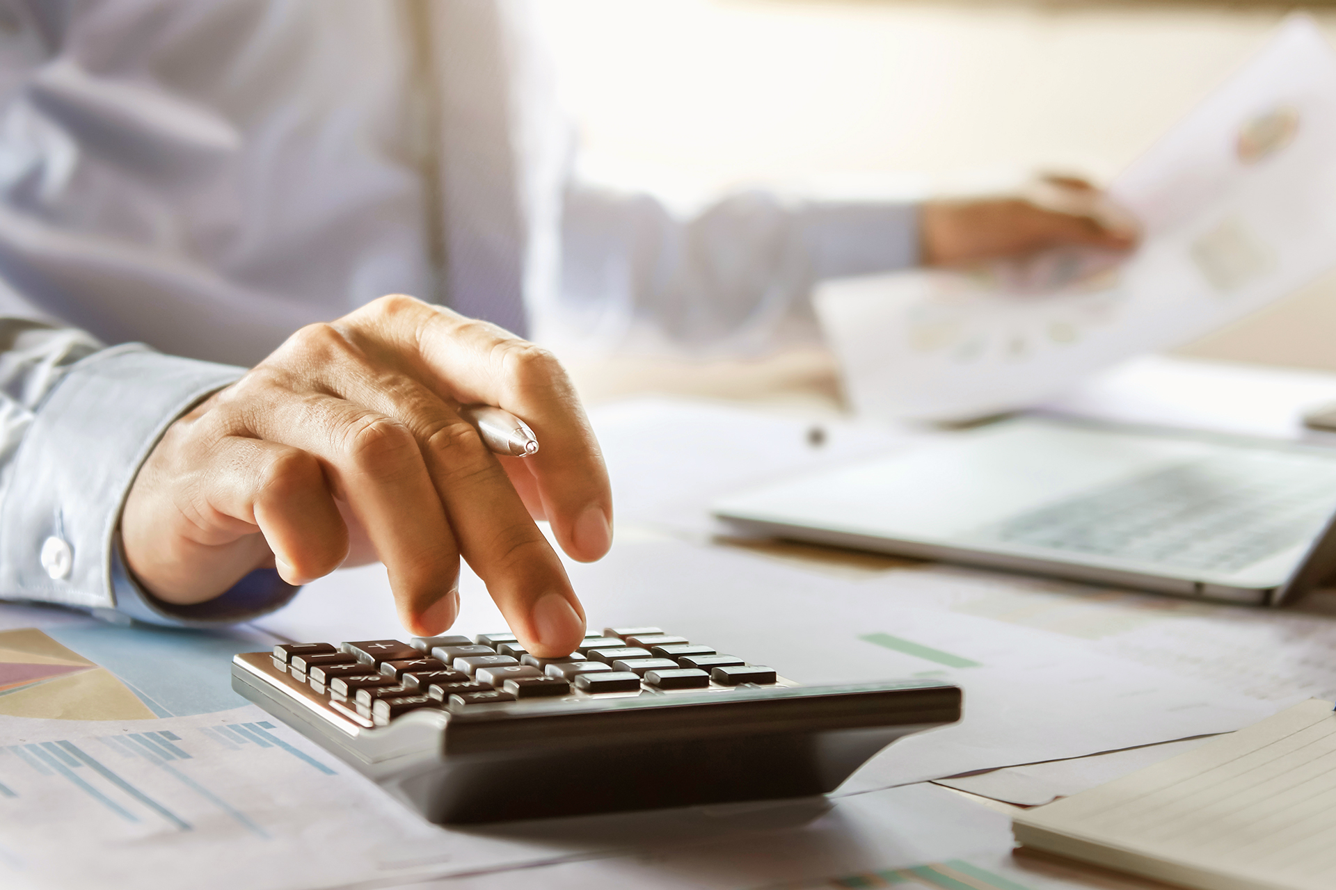 Mãos do empreendedor trabalhando com papeis e calculadora.